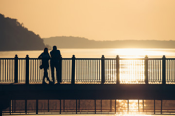 Couple in love at sunset on the pier, Baltic sea. Romantic evening promenade. Date at the sea. Travelling together.