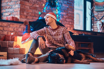 Stylish man playing with his cute dog in a decorated living room at Christmas time.