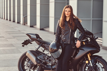 Obraz na płótnie Canvas A beautiful biker girl leaning on her superbike outside a building.
