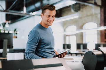 Joyful handsome young man using tablet and working in his own typography