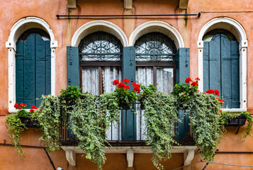 Fototapeta na wymiar tall windows on an old balcony with flowers in italy