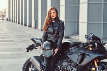 Fototapeta na wymiar A beautiful biker girl holding helmet while leaning on her superbike outside a building.