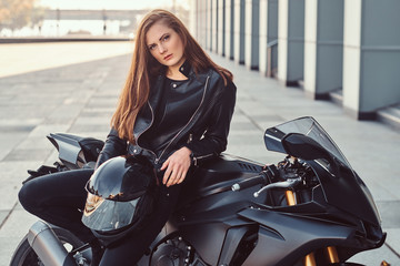 Fototapeta na wymiar A sexy biker girl posing on her superbike outside a building.