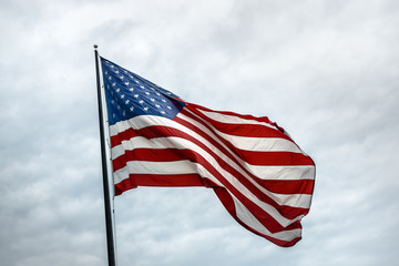 A large American flag flies against a cloudy white sky