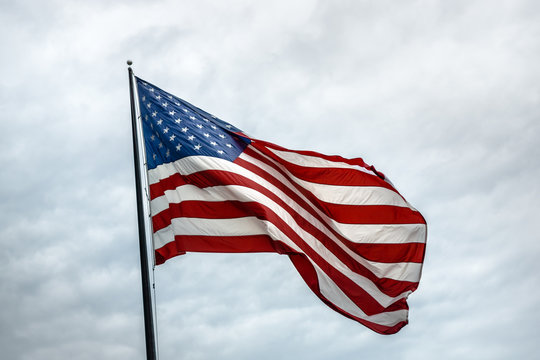 A Large American Flag Flies Against A Cloudy White Sky