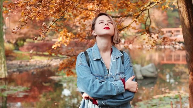 Footage of oung redhead girl in glasses and blue jeans jacket in a park. Autumn season time