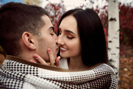 girl with white teeth and black hair holds the guy's face and stretches to kiss him.