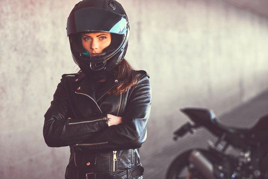 Close-up portrait of a biker girl with her arms crossed next to her superbike inside the bridge.