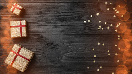 Wallpaper of winter holidays on black background. Gifts and gold stars. Space for text. Top view. Xmas greeting card with light bulb effect.