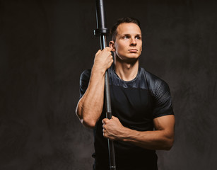 Portrait of a handsome young bodybuilder holding a barbell and looking at camera on dark background.