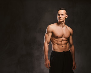 A handsome young fitness model with muscular body posing in studio on dark background.