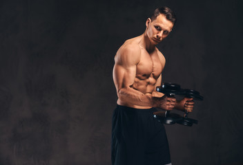 Fototapeta na wymiar Young shirtless bodybuilder with muscular body doing exercise with dumbbells on dark background.