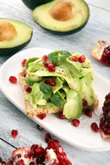 sliced avocado and ripe pomegranates on toast bread with spices and avocado.