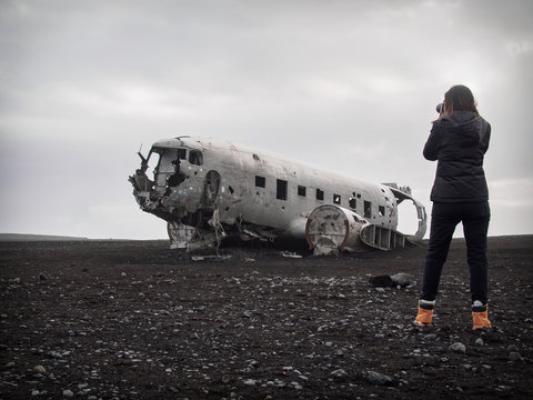 Girl is taking picture of abandoned crashed plane in Iceland in black sand desert
