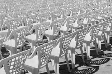 Vacant empty plastic white chairs pattern. White plastic chairs texture. Isolated View White Plastic Event Chairs Seating in Rows, Copy Space Use Overlay for Text. Black and white contrast made by sun