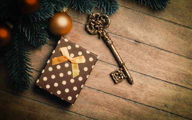 Christmas tree branch with toy balls and gift on wooden table.