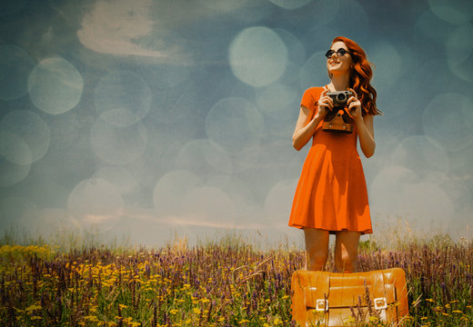 photo of the beautiful young woman with  camera and suitcase in the field