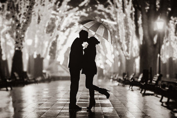Couple with umbrella kissing at night alley. Image in back and white color style