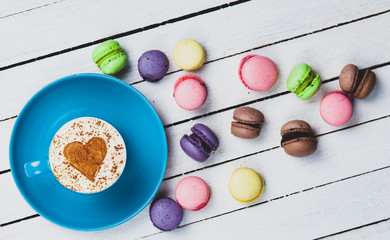 Cup of Cappuccino with heart shape symbol and macaron on white wooden background