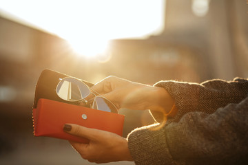 Closeup shot of woman hand opening red sunglasses case at the background of sun. Space for text