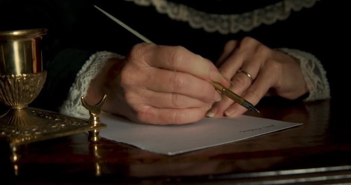 Lit by morning or evening sunlight the aged hands of an old Caucasian woman from the Victorian era using a dip pen starts writing a letter.