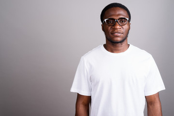 Young African man wearing white shirt and eyeglasses against gra