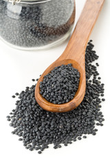 Heap of black organic beluga lentils in wooden spoon with black beluga lentils in storage jar on white