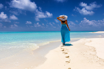 Frau im blauem Kleid läuft an einem tropischen Strand und genießt ihren Urlaub