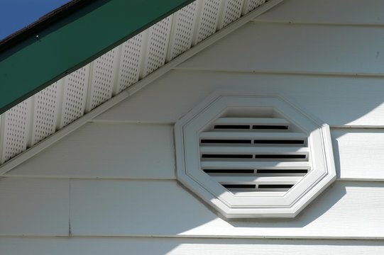 close up of white vinyl siding with air vent, soffit, and green fascia