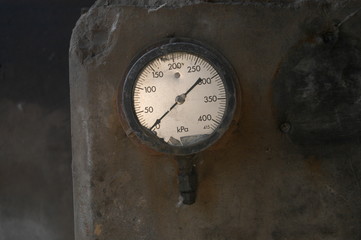 Close up of old, rusty pressure dial meter, on concrete wall