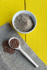 wooden spoon with flax seeds, linen flour and linen napkin on a yellow rustic table