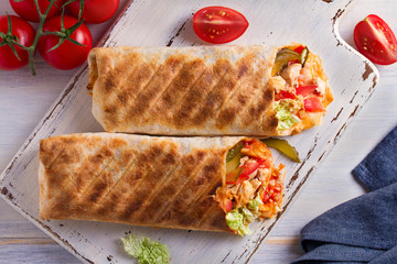Chicken wraps with tomatoes, pickles, cabbage and onion on white chopping board and wooden table. Tortilla, burritos, sandwiches, twisted rolls