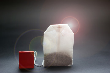 Tea in a paper bag with a red label, on a dark background. Herbal sachet, toned