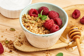 Homemade granola and yogurt in a bowl with raspberries on a wooden table.