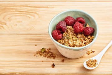 Homemade granola in a bowl with raspberries on a wooden table.