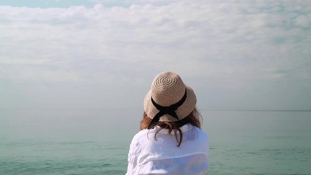 Rear view of unrecognizable caucasian woman wearing hat and white shirt looking at sea. Locked down real time medium shot