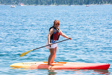 Active fit woman (20s) rows on a stand up paddleboard on Lake Tahoe in the summer.