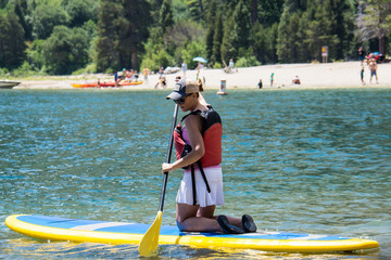 Active fit woman (30s) kneels on a stand up paddleboard on Lake Tahoe in the summer.