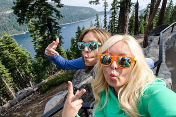 Two young adult woman take a selfie at Lake Tahoe Emerald Bay, wearing beach sunglasses and making...