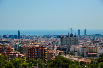 Barcelona city with high-rise buildings, tower cranes and blue sea in the background