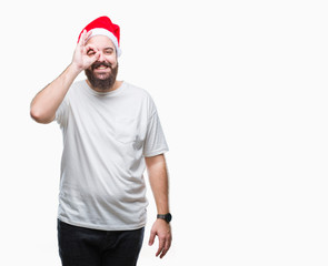 Fototapeta premium Young caucasian hipster man wearing christmas hat over isolated background doing ok gesture with hand smiling, eye looking through fingers with happy face.
