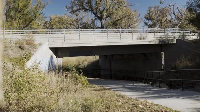 An establishing shot of a highway overpass with a very nice cycling and jogging path running underneath it being used by a cyclist.