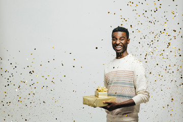 Portrait of a happy young man with a big smile holding gifts as golden confetti are falling