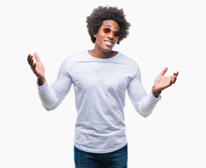 Afro american man wearing sunglasses over isolated background clueless and confused expression with arms and hands raised. Doubt concept.