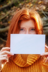 Purtrait schöner junger Frau mit roten Haaren, gGinger, die lächelnd ein leeres unbeschriebenes Papier in beiden Händen hält, Textfreiraum, platz für Ihren Text.