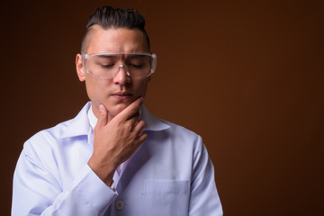 Young handsome multi-ethnic man doctor against brown background