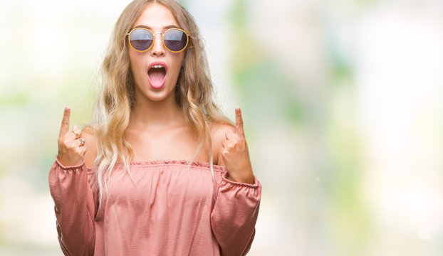 Beautiful young blonde woman wearing retro sunglasses over isolated background amazed and surprised looking up and pointing with fingers and raised arms.