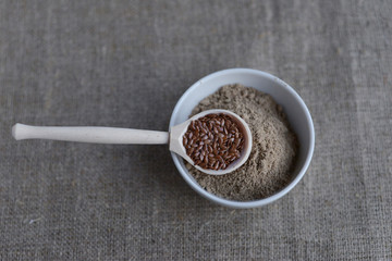 a bowl of flax flour and a wooden spoon with flax seeds on linen canvas
