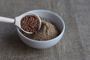 a bowl of flax flour and a wooden spoon with flax seeds on linen canvas