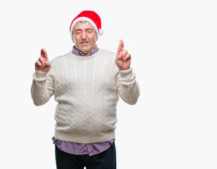 Handsome senior man wearing christmas hat over isolated background smiling crossing fingers with hope and eyes closed. Luck and superstitious concept.